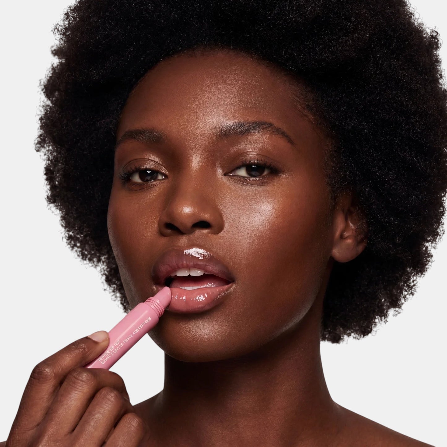 Model brengt SOLA-GLOW Sola lip tint aan voor een glanzende, gehydrateerde look met een zachtroze kleur.